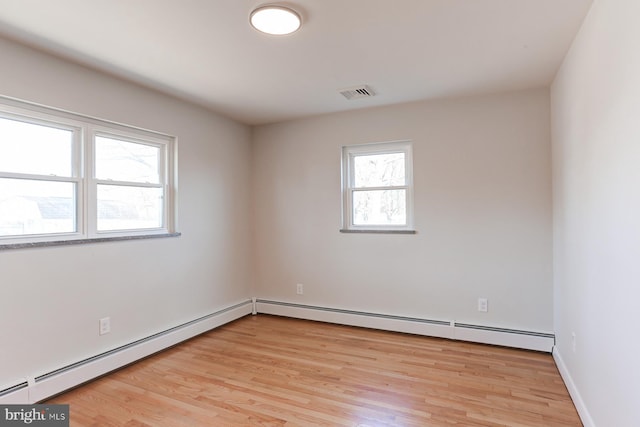 empty room with a baseboard heating unit, baseboards, visible vents, and light wood finished floors