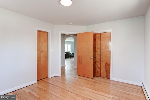 empty room with a baseboard radiator, baseboards, arched walkways, and light wood-style flooring