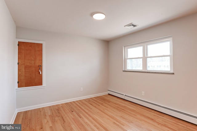 empty room featuring light wood finished floors, visible vents, a baseboard heating unit, and baseboards