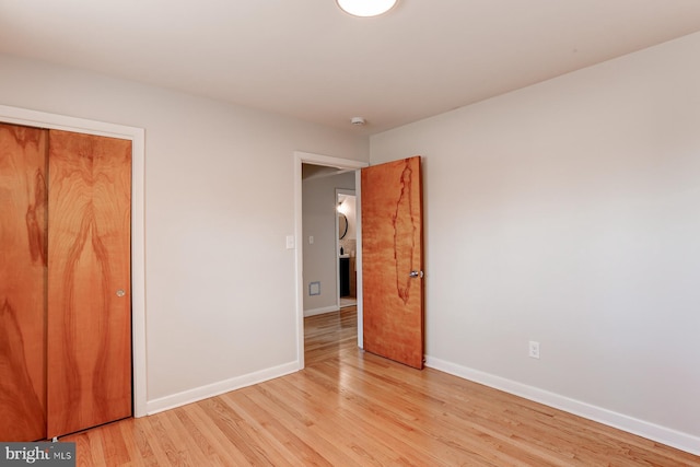 unfurnished bedroom featuring light wood-style floors, baseboards, and a closet