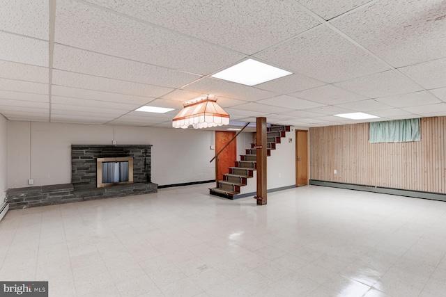 finished basement featuring a baseboard heating unit, stairway, a drop ceiling, a stone fireplace, and tile patterned floors