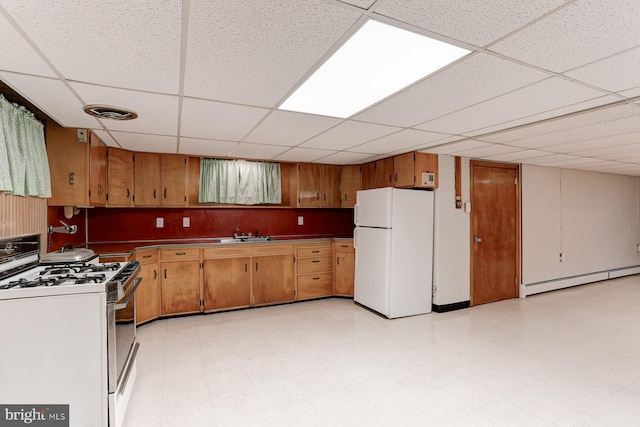 kitchen featuring a baseboard heating unit, gas range oven, freestanding refrigerator, brown cabinetry, and light floors