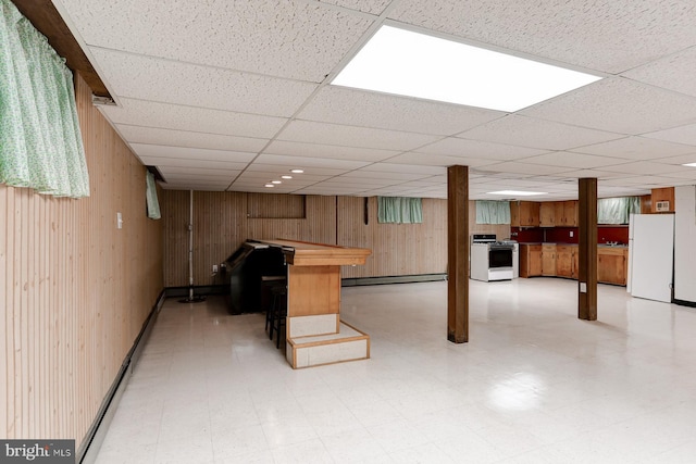 finished basement featuring light floors, wood walls, freestanding refrigerator, and a baseboard radiator