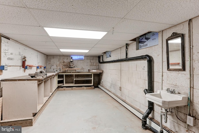 basement with a drop ceiling, a workshop area, concrete block wall, and a sink