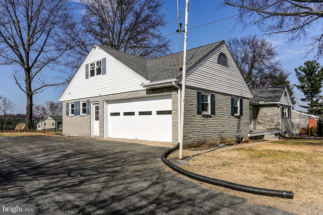 view of home's exterior featuring stone siding, driveway, a garage, and roof with shingles