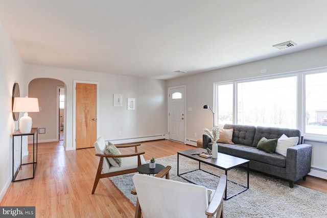 living area with a baseboard radiator, arched walkways, and light wood finished floors