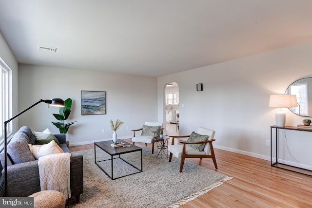 living area featuring arched walkways, visible vents, baseboards, and wood finished floors