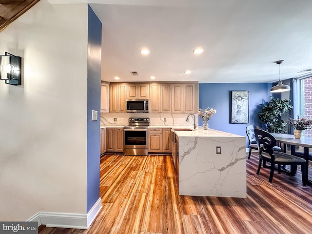 kitchen with light wood-style flooring, a sink, tasteful backsplash, appliances with stainless steel finishes, and a peninsula