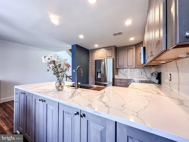 kitchen with a sink, decorative backsplash, light stone counters, and appliances with stainless steel finishes