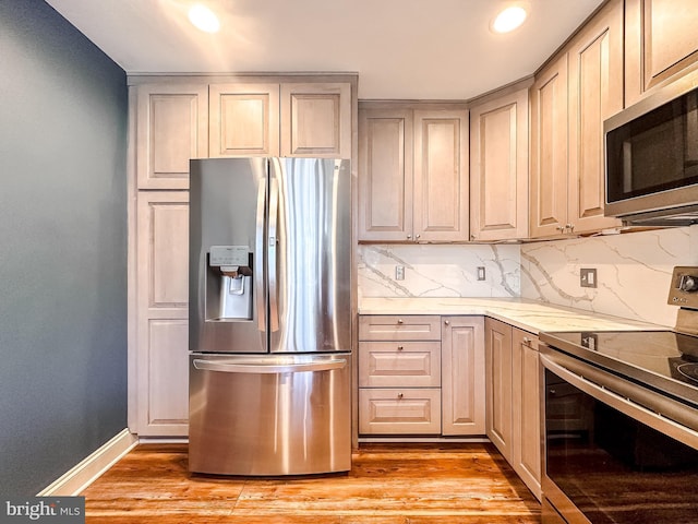 kitchen featuring light stone countertops, baseboards, light wood finished floors, decorative backsplash, and appliances with stainless steel finishes