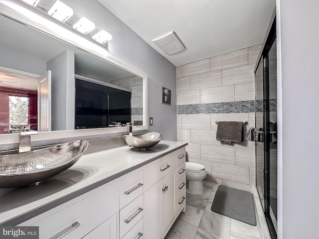 full bathroom with a sink, toilet, tile walls, and double vanity