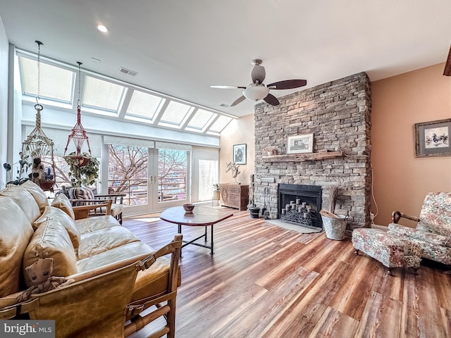 living area featuring wood finished floors, visible vents, vaulted ceiling with skylight, ceiling fan, and a stone fireplace