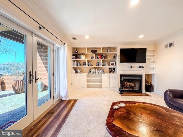 carpeted living area with visible vents, french doors, crown molding, and a fireplace with flush hearth