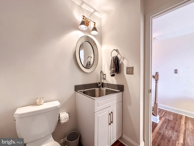 half bath with vanity, toilet, wood finished floors, and baseboards