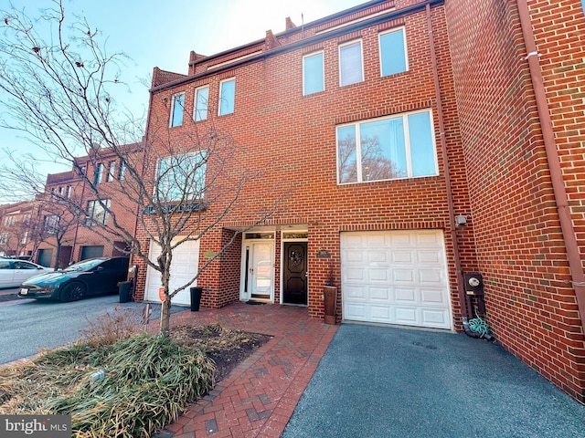 townhome / multi-family property featuring aphalt driveway, brick siding, and a garage