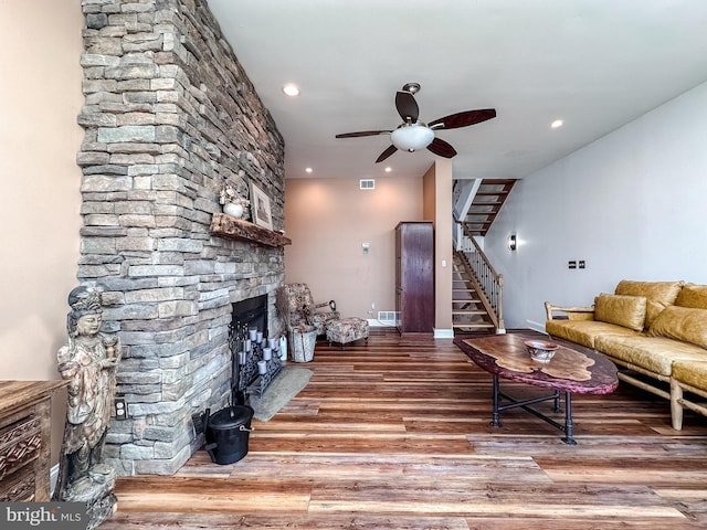 living area with visible vents, a ceiling fan, wood finished floors, a stone fireplace, and stairs