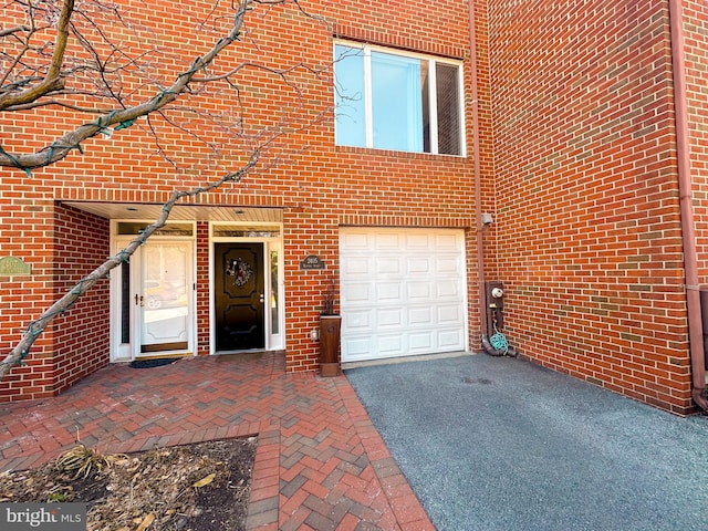 entrance to property featuring aphalt driveway, an attached garage, and brick siding