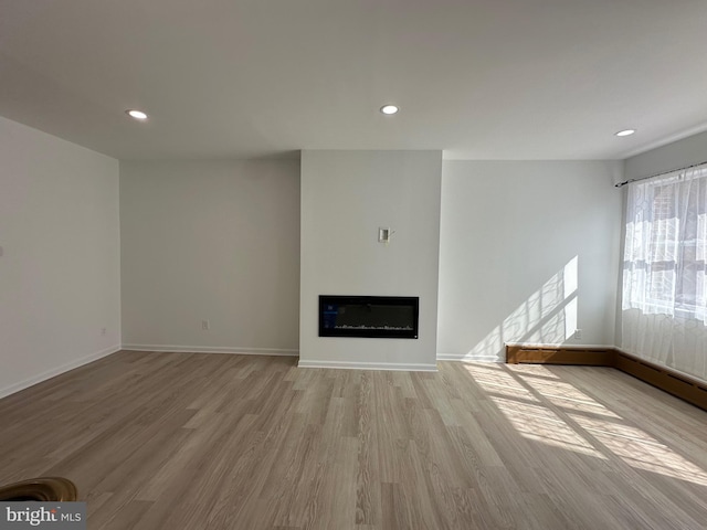 unfurnished living room featuring recessed lighting, baseboards, a glass covered fireplace, and light wood finished floors