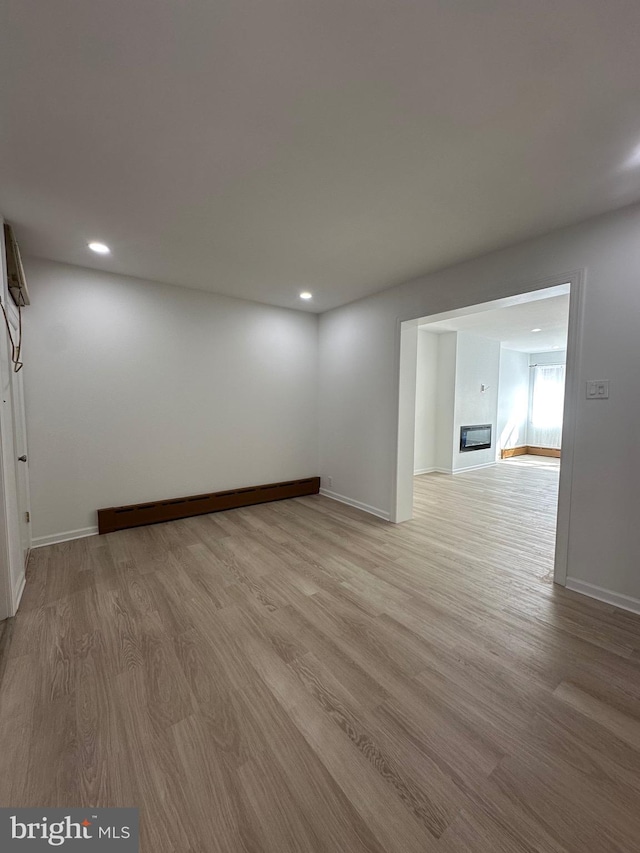 spare room featuring a baseboard heating unit, recessed lighting, baseboards, and light wood-type flooring