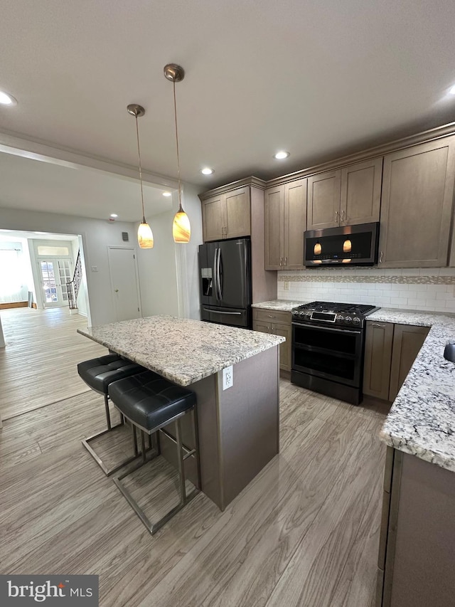 kitchen with a kitchen island, light stone countertops, a breakfast bar area, decorative backsplash, and appliances with stainless steel finishes