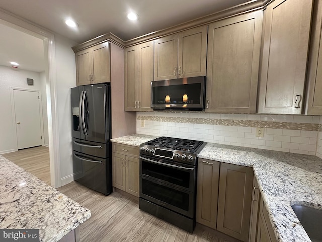 kitchen with light stone counters, backsplash, recessed lighting, stainless steel appliances, and light wood finished floors