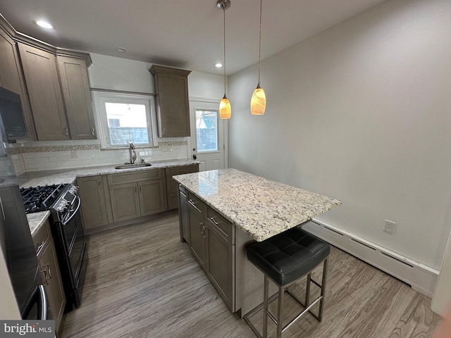 kitchen featuring double oven range, light wood finished floors, a sink, decorative backsplash, and a baseboard heating unit