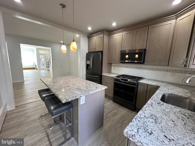 kitchen with light wood finished floors, a sink, stainless steel appliances, a kitchen breakfast bar, and backsplash