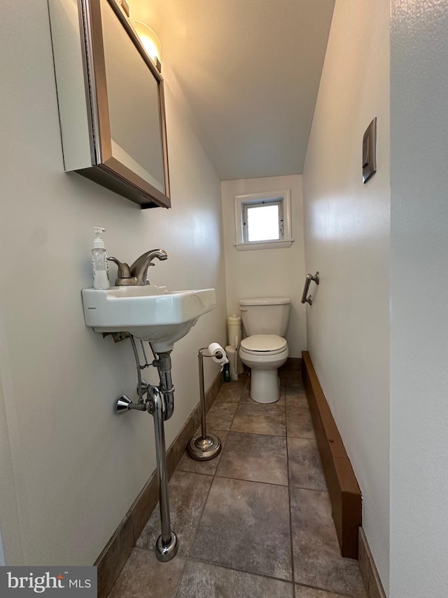 half bath featuring a sink, baseboards, toilet, and tile patterned flooring