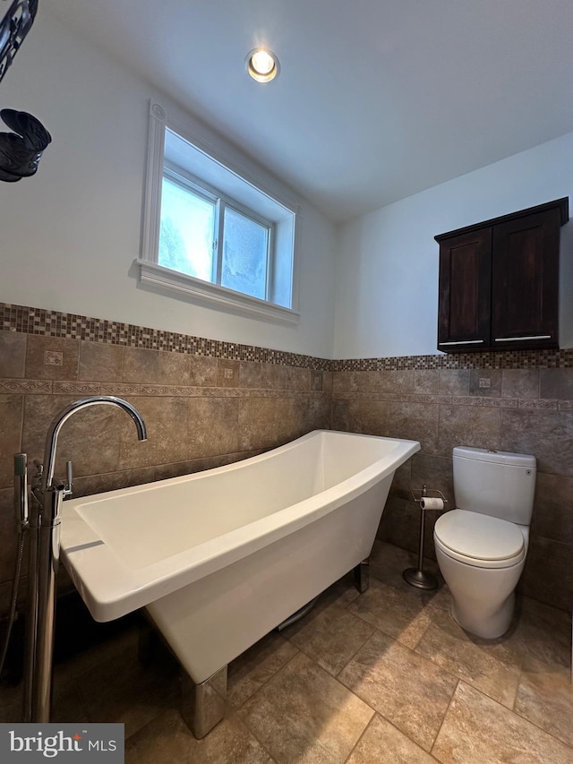 full bath with a wainscoted wall, a freestanding tub, recessed lighting, tile walls, and toilet