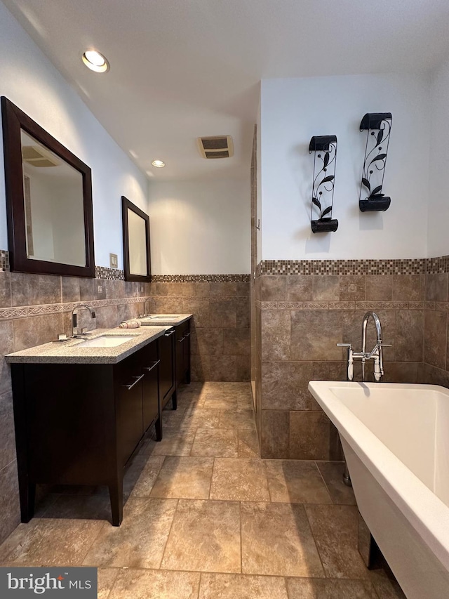 full bathroom with a sink, a freestanding tub, tile walls, and double vanity