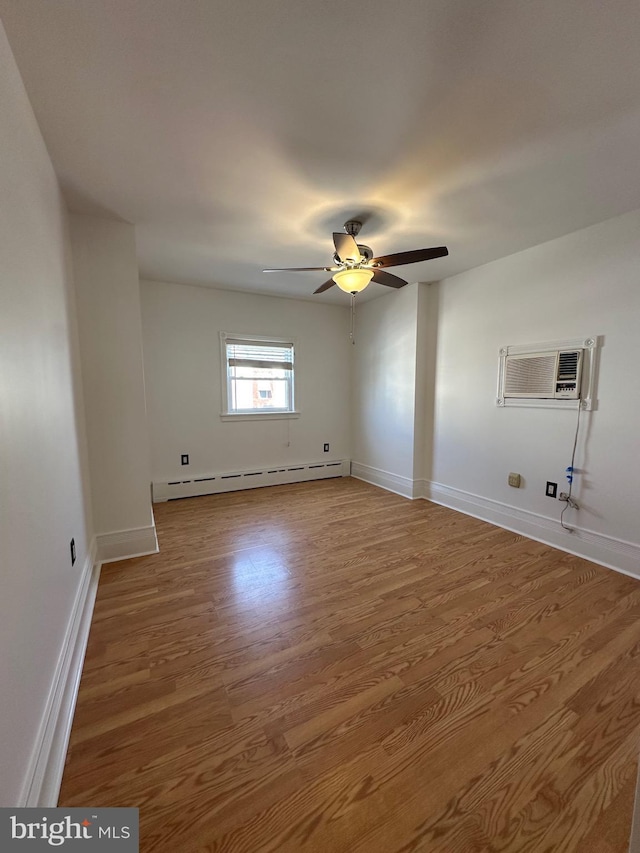 spare room with a baseboard heating unit, baseboards, a wall unit AC, wood finished floors, and a ceiling fan