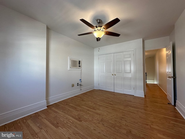 unfurnished bedroom featuring wood finished floors, baseboards, a closet, and a wall mounted AC