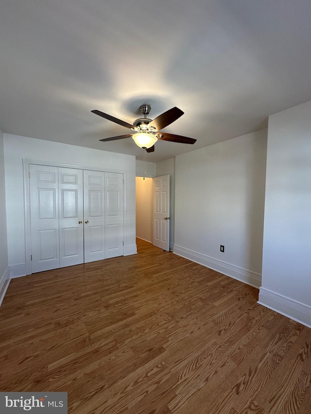 unfurnished bedroom with a closet, baseboards, wood finished floors, and a ceiling fan