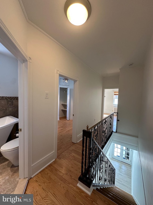 corridor featuring baseboards, an upstairs landing, wood finished floors, and crown molding