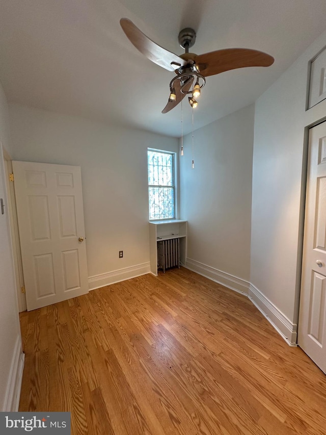 empty room featuring light wood-type flooring, baseboards, radiator, and ceiling fan