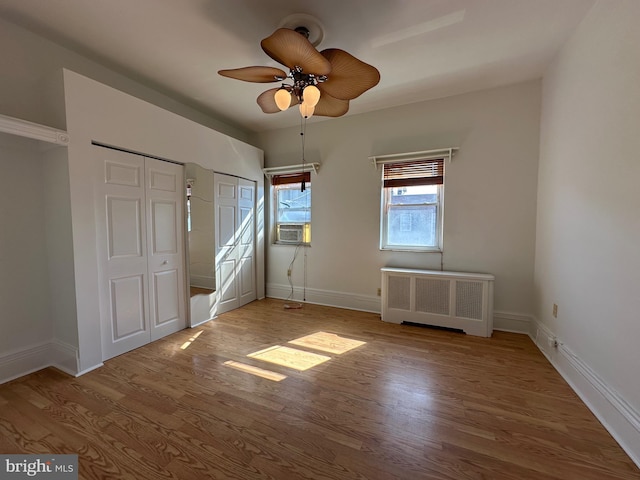 unfurnished bedroom featuring radiator, a ceiling fan, wood finished floors, baseboards, and two closets