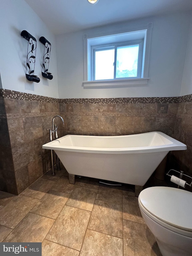 bathroom featuring toilet, tile walls, wainscoting, and a soaking tub