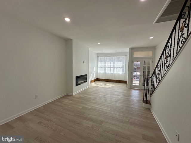 unfurnished living room featuring a glass covered fireplace, stairway, baseboards, and wood finished floors