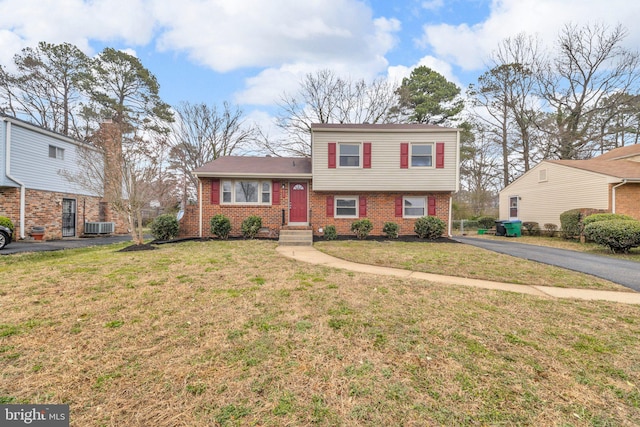 tri-level home featuring aphalt driveway, central AC unit, brick siding, and a front yard