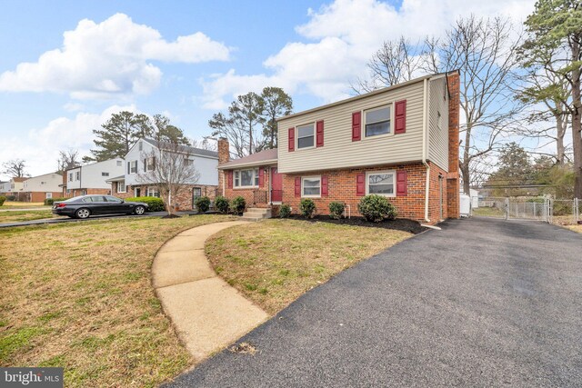 split level home featuring aphalt driveway, brick siding, a front yard, and a chimney