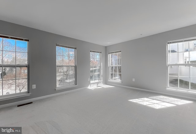 carpeted empty room featuring visible vents, plenty of natural light, and baseboards