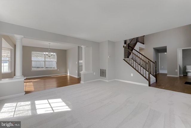 unfurnished living room with visible vents, ornate columns, carpet floors, stairs, and a notable chandelier