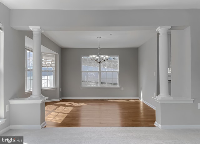 unfurnished dining area with a notable chandelier, decorative columns, and wood finished floors