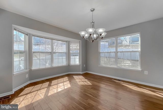 unfurnished dining area with a notable chandelier, wood finished floors, visible vents, and baseboards