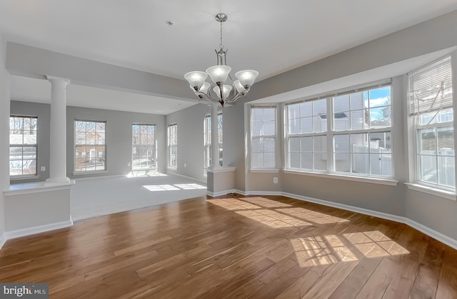 unfurnished dining area featuring decorative columns, wood finished floors, and baseboards