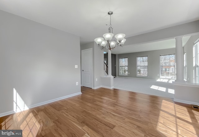 unfurnished dining area featuring visible vents, baseboards, an inviting chandelier, wood finished floors, and ornate columns