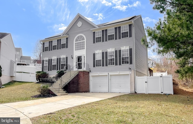 colonial inspired home with a gate, fence, solar panels, concrete driveway, and a garage