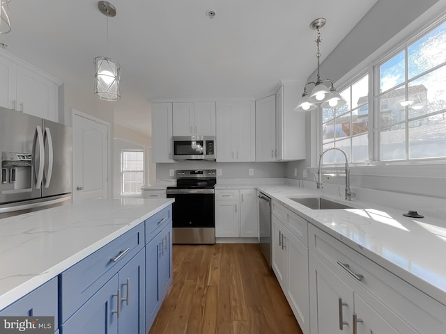 kitchen featuring stainless steel appliances, wood finished floors, white cabinetry, blue cabinets, and a sink