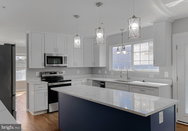 kitchen with wood finished floors, a sink, white cabinets, appliances with stainless steel finishes, and decorative light fixtures