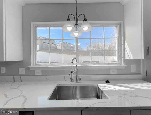 kitchen with an inviting chandelier, white cabinets, light stone counters, and a healthy amount of sunlight